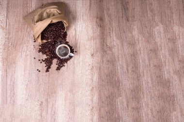 Kahve çekirdeği yığını üzerinde bir fincan kahve, ahşap masada.