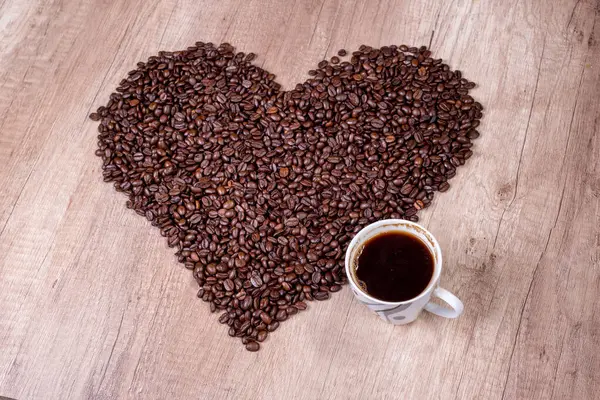 Cup with coffee and heart from coffee beans on wooden background,retro