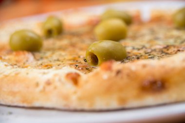 Peynirli ve zeytinli pizza, beyaz tabakta servis edilir, yakın.