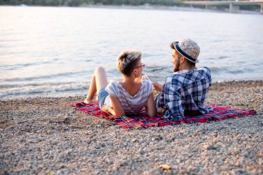 Çift kumsalda, bir battaniyenin üzerinde yatıyor.