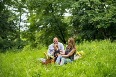 Genç bir aile çayırda piknik yapıyor.