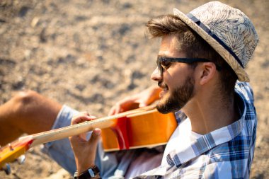 Hippi çocuk plajda gitar çalıyor.
