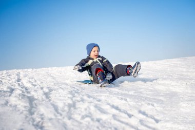 Çocuk karda eğleniyor, kızakla kayıyor.