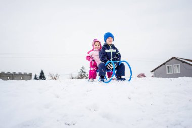Gülümseyen çocuklar kar kaplı tepede kızak kaymaya hazırlanıyor..