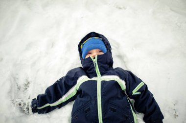 Karda sırt üstü uzanmış, kar meleği yapan küçük bir çocuk..