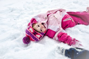 Karda uzanmış tatlı küçük kız, kar meleği yapıyor ve gülümsüyor..
