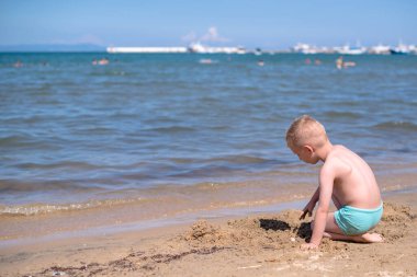 Çocuk kumsalda oturuyor ve kumsalda oynuyor.