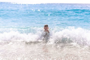 Bir çocuk güzel, çakıllı sahilde suda oynuyor.