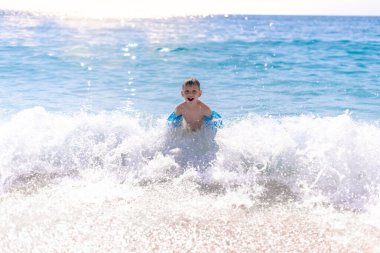 Bir çocuk güzel, çakıllı sahilde suda oynuyor.