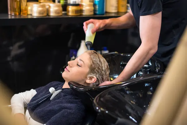 Kuaför sarışın kızların saçını yıkıyor.