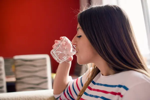 Kız odada bir bardak suyun tadını çıkarıyor.