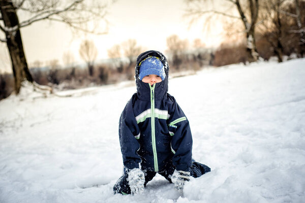 Cute boy sitting in snow after falling, looking at camera.