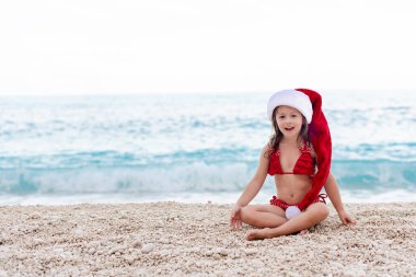 Güzel çakıl taşlı sahilde Noel Baba şapkalı mutlu küçük kız..