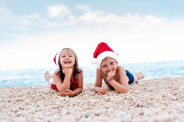 Suyun kenarında oturan Noel Baba şapkalı abla ve kardeş. Modern Noel kutlaması