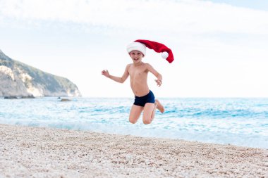 Noel Baba şapkalı mutlu çocuk sahilde Noel 'i kutluyor.