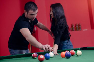 Adam kıza bilardo oynamayı öğretiyor.
