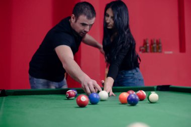 Adam kıza bilardo oynamayı öğretiyor.