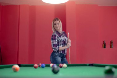 Attractive young blond girl is playing billiard clipart
