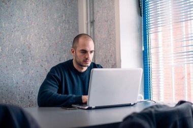 Genç işadamı ofiste dizüstü bilgisayar kullanıyor, okuyor ve daktilo yazıyor..