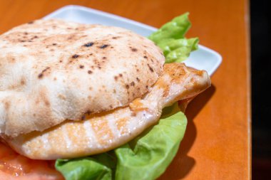 Tavuk göğlü hamburger, ahşap masada marul ve domates..