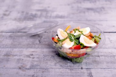 Yumurta ve yaprak sebzeli taze bitki salatası, plastik salata yayıyla servis edilir..
