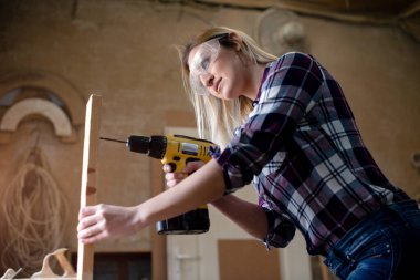 Genç ve çekici sarışın kadın marangoz atölyesinde çalışıyor.