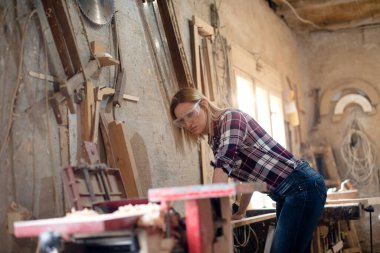 Genç ve çekici sarışın kadın marangoz atölyesinde çalışıyor.