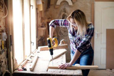 Genç ve çekici sarışın kadın marangoz atölyesinde çalışıyor.