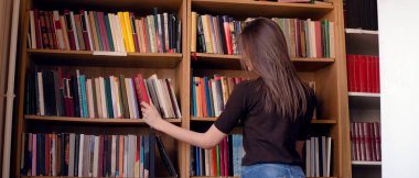 Kitap rafından, dikiz aynasından kitap alan kadın görüntüsü.