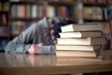 Üniversite kütüphanesinde uyuyan bitkin öğrenci, kitapları kapat..