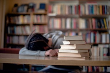 Kütüphanede uyuyan yorgun öğrenci, masanın üstünde kitaplar, ön plana odaklan..
