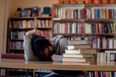 Üniversite öğrencisi kafasını kütüphane masasında dinlendiriyor..