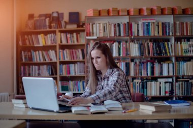 Kütüphanede dizüstü bilgisayarla çalışan, internete yaslanan genç bir kadın..