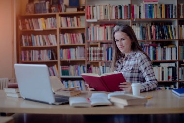 Kütüphanede dizüstü bilgisayar ve kitap kullanarak öğrenen kendinden emin bir kız öğrencinin portresi.