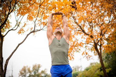Sporcu esneme egzersizleri yapıyor, eller havada, yukarı bakıyor..