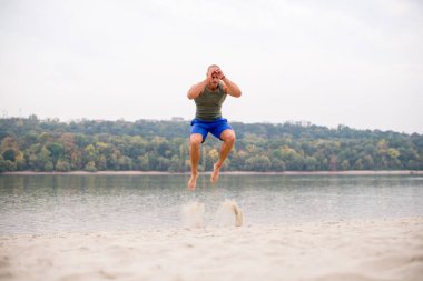 Genç adam güzel bir yaz gününde kumda zıplıyor..