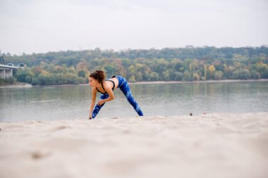 Genç bir kadın kumsalda esniyor, spor eğitimini tamamlıyor..