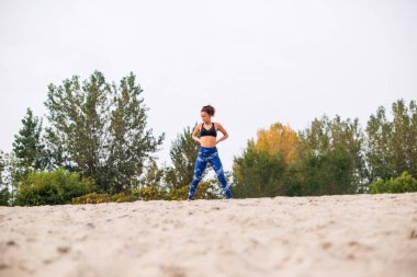 Beyaz kadın sporcu, kumların üzerinde duruyor, el ele tutuşuyor ve aşağıya bakıyor..