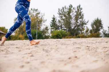 Kumsalda koşan, mavi koşu pantolonu giyen ve yalın ayaklı bir kadın..