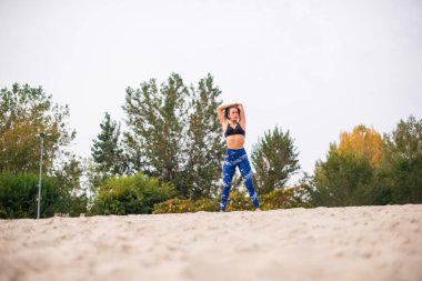 Genç bir kadın doğada esneme egzersizleri yapıyor, gözlerini kaçırıyor..