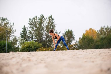 Kadın dışarıda egzersiz yapıyor, kumsalda geriniyor..