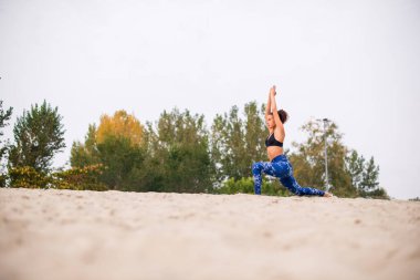Kum üzerinde denge egzersizleri yapan kadın, el kaldırılmış..