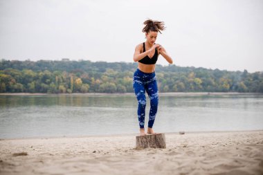 Kadın sporcu plajda egzersiz yapıyor, kütüğün üstünde zıplıyor..