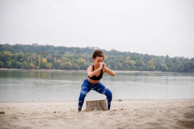 Kumsalda egzersiz yapan, çömelme hareketleri yapan bir kadın..