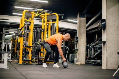 Spor salonundaki adam kettlebell ile salıncak egzersizi yapıyor.