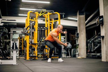 Spor salonundaki adam kettlebell ile salıncak egzersizi yapıyor.