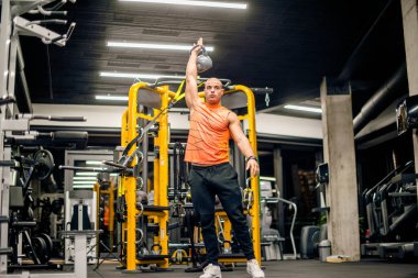 Spor salonundaki adam kettlebell ile salıncak egzersizi yapıyor.