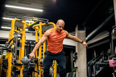 Spor salonundaki adam kettlebell ile salıncak egzersizi yapıyor.