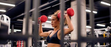 Çekici genç bayan spor salonunda küçük kırmızı ağırlıklarla antrenman yapıyor.