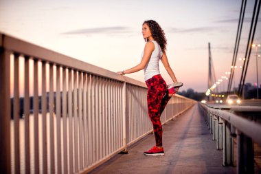 Dişi sporcu bacaklarını açık havada, köprüde açıyor.